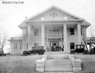 Historic mansion with cars and people on front steps in black and white photo