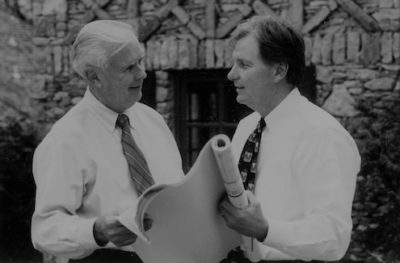 Two men discussing architectural plans outside a brick building