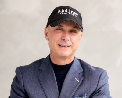 Man in blue blazer and black hat smiling at camera in front of neutral background