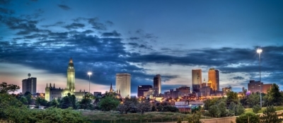 City skyline at dusk with illuminated buildings and a cloudy blue sky in the background.