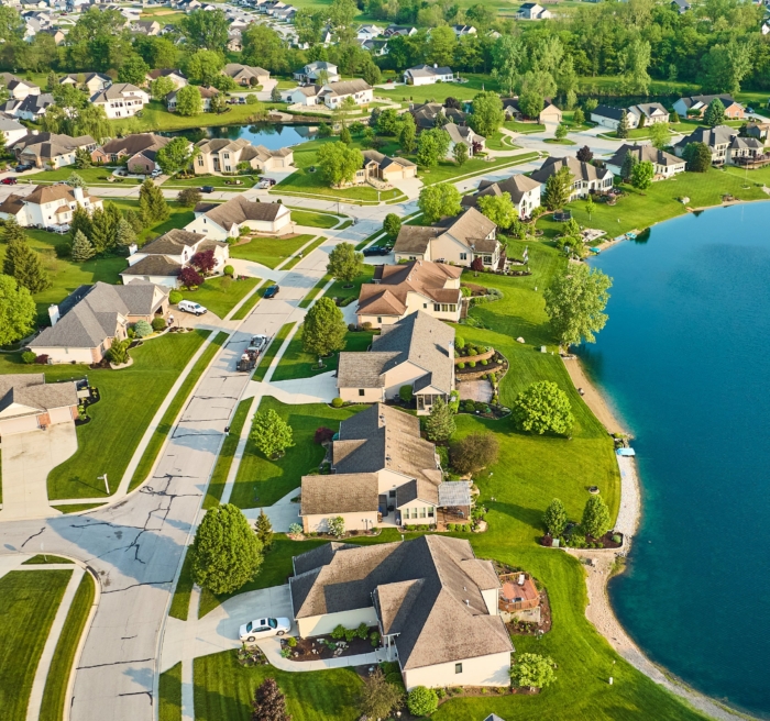Aerial view of suburban neighborhood with houses, green lawns, and a pond on a sunny day