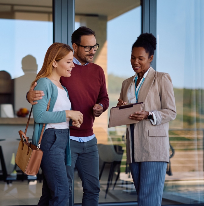 Couple consults with real estate agent outside modern home