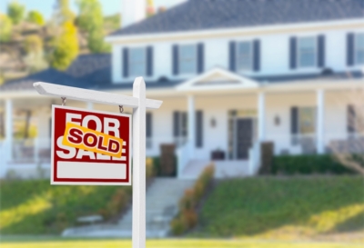 Sold sign in front of a large white house indicating successful real estate sale