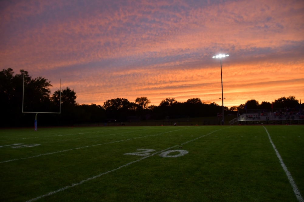 Football field at sunset with glowing sky and stadium lights on