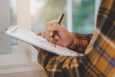 Person in plaid shirt writing on a clipboard by a window