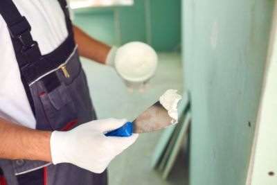 Person in overalls applying spackle on wall with putty knife