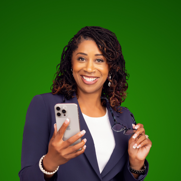 Smiling woman in a blazer holding a smartphone and glasses against a green background