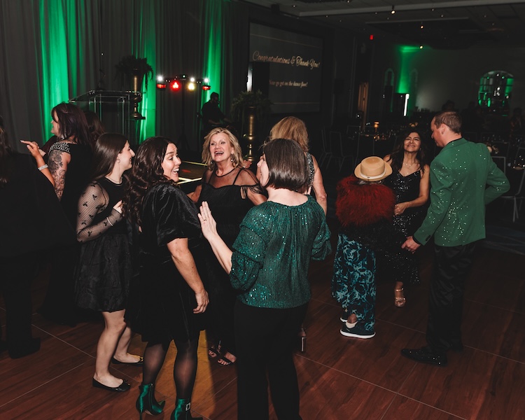 People dancing at a party with green and black attire in an indoor venue with green lighting.