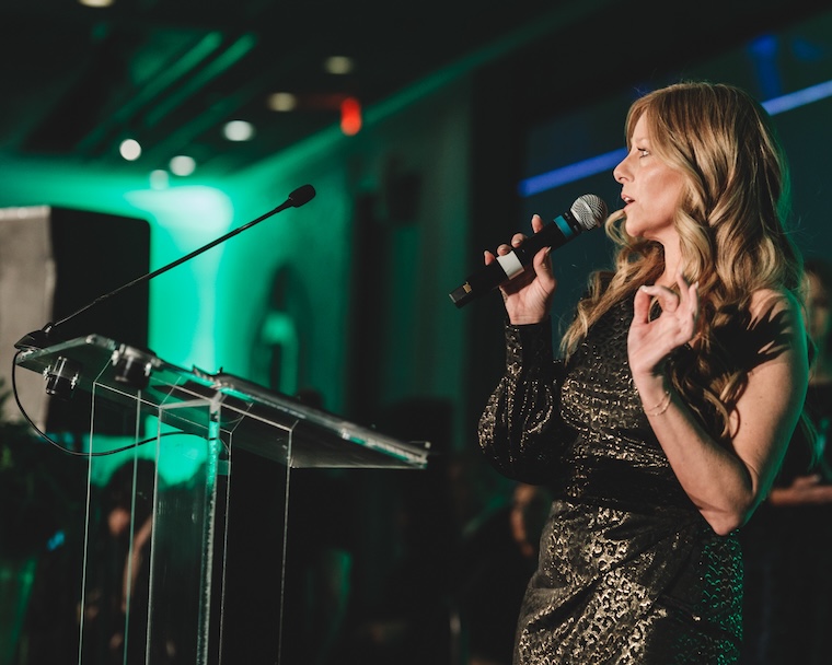 Woman speaking on stage with microphone in elegant dress at event