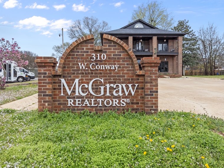 Red brick sign for McGraw Realtors at 310 W. Conway with a building in the background.
