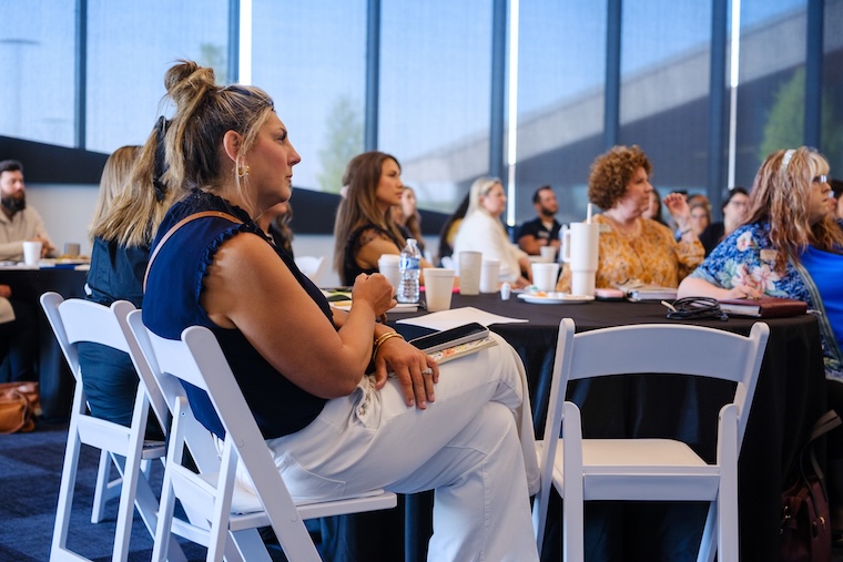 People attentively listening at a conference in a modern, well-lit venue with large windows.