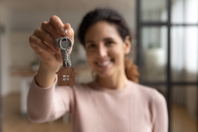 Smiling woman holding a house key in a bright home interior